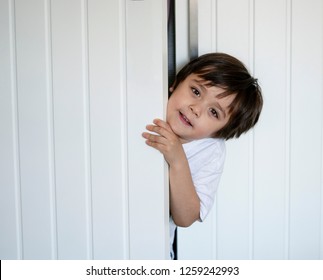 Cropped Shot Happy Boy Playing Hide And Seek  In Wardrobe, Active Kid Looking Out While Hiding Behind The White Door, Child With Happy Face Having Fun Playing Hind And Seek Inside Closet, Positive Kid