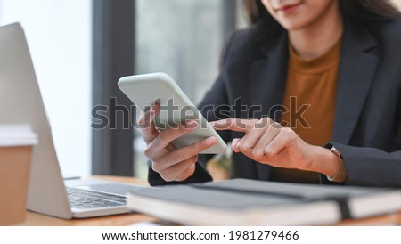Cropped shot of happy businesswoman using smart phone while sitting in modern office.