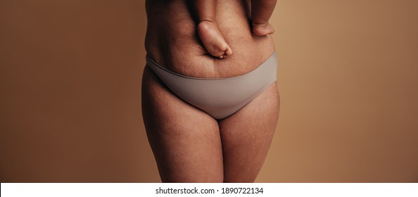 Cropped shot of a healthy female carrying her baby. Close-up of a woman in underwear with feet of child on postnatal belly.
