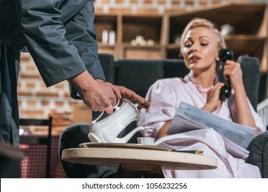 Cropped Shot Of Husband Pouring Coffee To Woman Reading Newspaper And Talking By Vintage Telephone, 1950s Style  