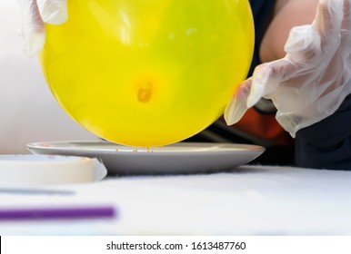 Cropped Shot Kid Hand Holding Balloon Above Plate Of Dry Gelatin Crystals, School Kid Doing Science Project, Experiment With Gelatine And Static Charged Balloon, Science Experiment Concept