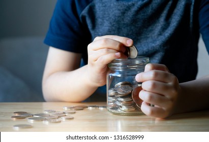 Cropped Shot Kid Hand Putting Money Coins Into Clear Jar,  Child Counting His Saved Coins, Childhood Hand Holding Coin, Children Learning About Saving For Future Concept