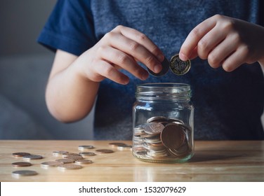 Cropped Shot Kid Hand Putting Money Coins Into Clear Jar,  Child Counting His Saved Coins, Childhood Hand Holding Coin, Children Learning About Saving For Future Concept