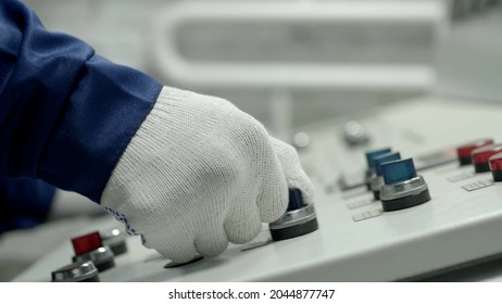 Cropped shot of machine operator hand turns on control panel of industrial machine. Close up of technician in gloves push button on control pannel 