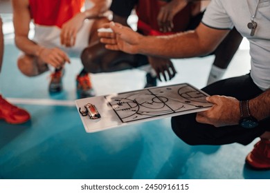 Cropped shot of a male basketball team and elderly coach in huddle while discussing game tactics. Planing the game tactic and teaching players defense. Focus on a coach clipboard with drawings on it. - Powered by Shutterstock