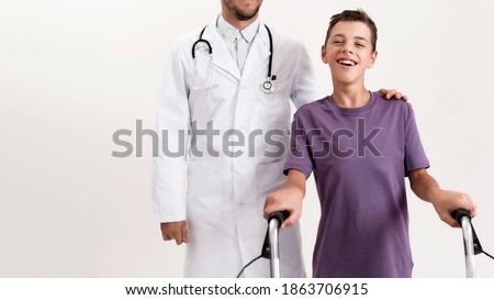 Cropped shot of male doctor helping teenaged disabled boy with cerebral palsy, taking steps using his walker isolated over white background. Children with disabilities and special needs. Web Banner
