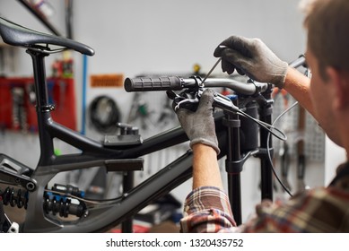 Cropped shot of male mechanic working in bicycle repair shop, serviceman repairing modern bike using special tool, wearing protective gloves - Powered by Shutterstock