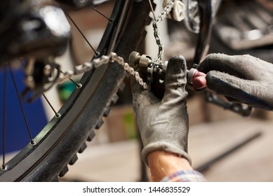 Cropped shot of male mechanic working in bicycle repair shop, worker repairing bike chain using special instrument, wearing protective gloves - Powered by Shutterstock