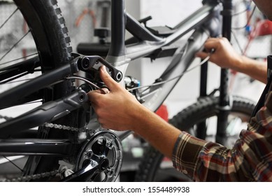 Cropped shot of male mechanic working in bicycle repair shop, repairman fixing bike in a workshop, wearing protective workwear - Powered by Shutterstock