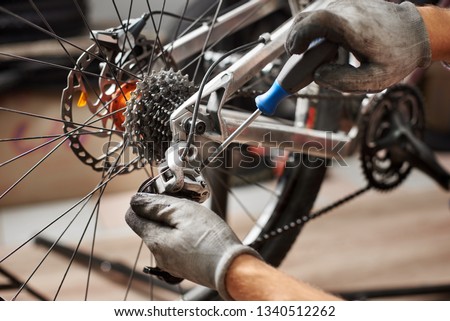 Cropped shot of male mechanic working in bicycle repair shop, mechanic repairing bike using special tool, wearing protective gloves
