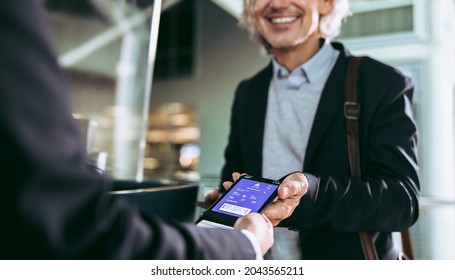 Cropped Shot Of A Male Passenger Check In At Airport Terminal Using Digital Flight Ticket. Businessman Showing Plane Boarding Pass To Staff On Mobile Phone.