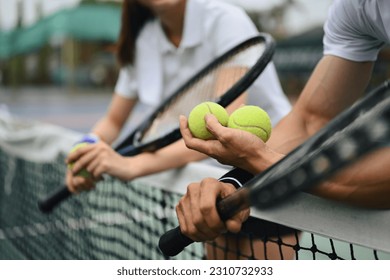 Cropped shot of male tennis coach hand holding balls, giving instructions to his student, standing by net at the court - Powered by Shutterstock