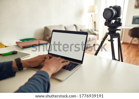 Cropped shot of male vlogger working on laptop while sitting at his workplace at home. Recording video blog. Focus on blank laptop screen. Freelance, blogging. Stay home, self isolation