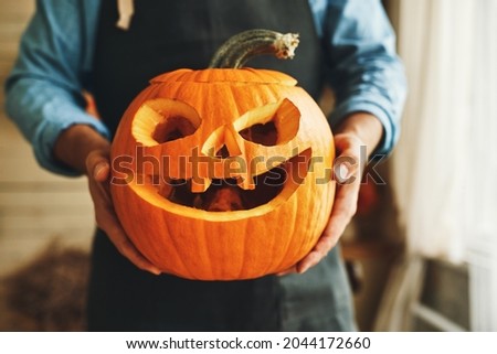 Cropped shot of man in apron with Halloween pumpkin monster in hands, person showing at camera classic carven spooky jack-o-lantern with big, gap-toothed grin, triangular eyes and nose