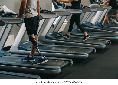 Cropped Shot Of Man With Artificial Leg Running On Treadmills At Gym With Other People