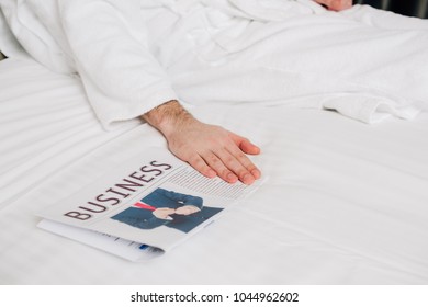 Cropped Shot Of Man In Bathrobe Lying On Bed With Business Newspaper