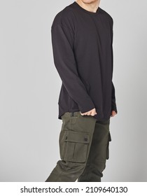 Cropped Shot Of Man In Black Blank Long Sleeved And Green Cargo Pants. Standing On Gray Background. Mockup For Print Or Design Template. Basic Clothing Line No Logo