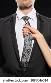 Cropped shot of a man in black jacket and white shirt. A female hand is holding man's classic tie made of gray silk with light flowers pattern. The man and the lady are outside the purview.            - Shutterstock ID 1897046314