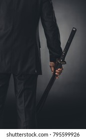 Cropped Shot Of Man In Business Suit With Katana Sword On Black