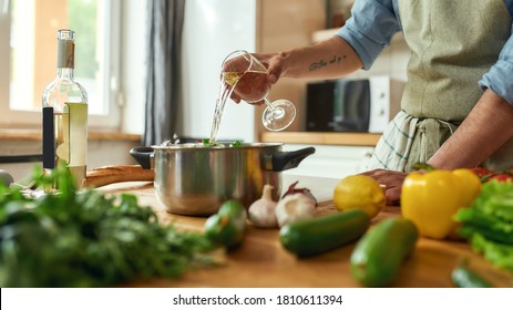 Cropped Shot Of Man, Chef Cook Pouring A Glass Of White Wine Into The Pan With Chopped Vegetables While Preparing A Meal In The Kitchen. Cooking At Home, Italian Cuisine. Selective Focus. Web Banner