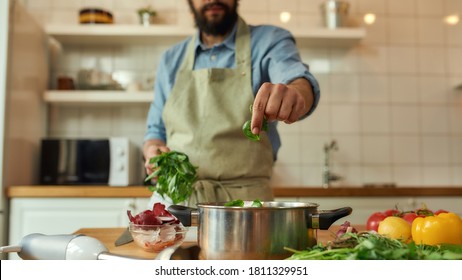 Cropped Shot Of Man, Chef Cook Adding Basil Leaf To The Pot With Chopped Vegetables While Preparing Healthy Meal, Soup In The Kitchen. Cooking At Home, Italian Cuisine. Focus On Hand. Web Banner