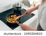 cropped shot of man cooking vegetables in frying pan on electric stove