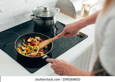 cropped shot of man cooking vegetables in frying pan on electric stove Stock Photo