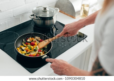 cropped shot of man cooking vegetables in frying pan on electric stove