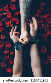 Cropped Shot Of Man Holding Handcuffs On Female Hands Above Black Fabric With Red Rose Petals