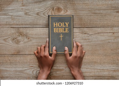 cropped shot of man holding holy bible on rustic wooden table