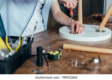 cropped shot of man repairing stool with screwdriver 
