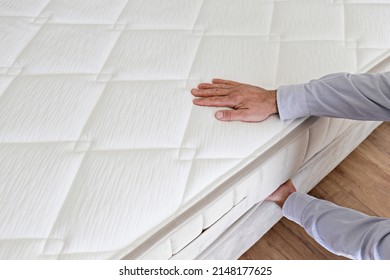 Cropped shot of man testing white orthopedic matress on firmness. Male pressing hypoallergenic foam mattresses surface to check its softness. Close up, copy space, top view, background.