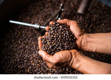 Cropped shot of a man's hands holding freshly roastd aromatic coffee beans over a modern machine used for roasting beans - Powered by Shutterstock