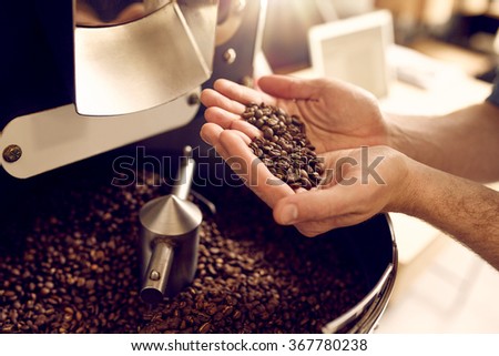 Cropped shot of a man's hands holding freshly roastd aromatic coffee beans over a modern machine used for roasting beans
