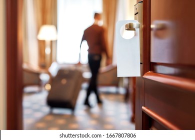 Cropped shot of middle-aged businessman in casual wear with suitcase entering his room in the background. A door with a sign at the front. Horizontal shot. Selective focus