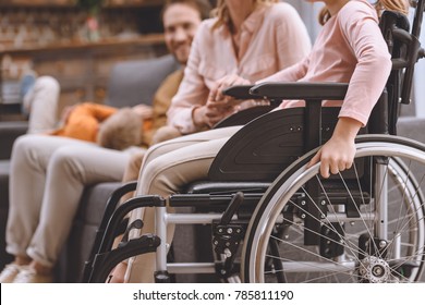 cropped shot of mother and daughter in wheelchair holding hands at home