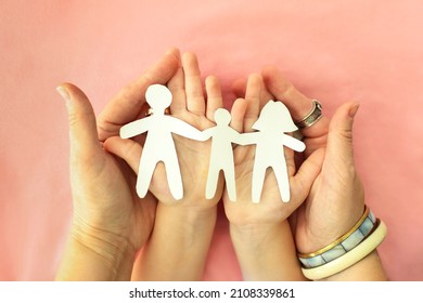 Cropped shot of mother, father and child holding family paper cut out in hands, isolated on pink background. cardboard figures of parents and kid holding hands together. International Day of Families