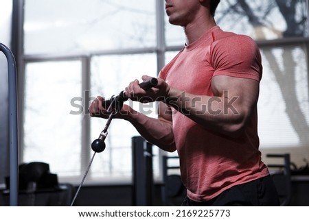 Cropped shot of a muscular bodybuilder doing bicep curls in cable crossover gym machine