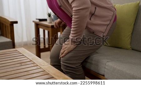 cropped shot of an old female dropping down back in the couch and rubbing her aching knees with hand while trying to get up from her seat in the living room 商業照片 © 