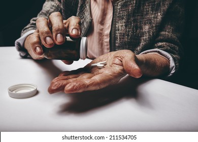 Cropped Shot Of A Old Woman Sitting At A Table Shaking A Pill Out Of A Pill Bottle. Focus On Hands. Senior Female Taking Medicine.