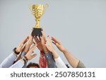 Cropped shot of people hands holding golden trophy cup. Team of joyful employees receiving business award, celebrating great work success. Professional achievement and collaborative success concept.