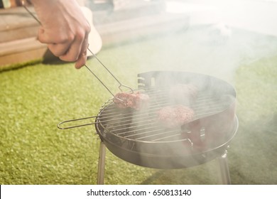 Cropped Shot Of Person Holding Tongs And Preparing Burgers On Outdoor Grill