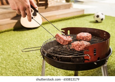 Cropped Shot Of Person Holding Tongs And Preparing Burgers On Outdoor Grill