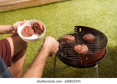 Cropped Shot Of Person Holding Tongs And Preparing Burgers On Outdoor Grill