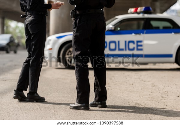 cropped shot of police officers standing in front of\
police car