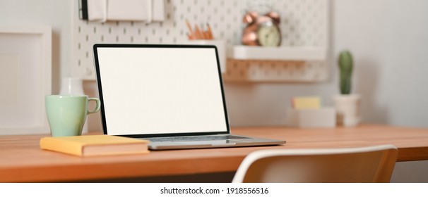 Cropped shot of portable workspace with laptop, notebook and mug on wooden table in home office, clipping path 