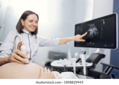 Cropped shot of a pregnant woman during ultrasound scanning at the fertility clinic. Female doctor pointing at the screen of ultrasound machine. Focus on ultrasound transducer on the pregnant belly - Powered by Shutterstock