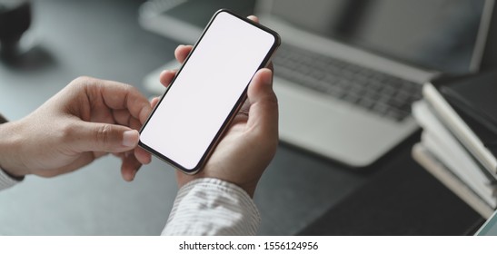 Cropped shot of professional businessman holding blank screen smartphone in dark modern office room - Powered by Shutterstock