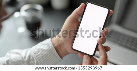 Cropped shot of professional businessman holding blank screen smartphone in dark modern office room