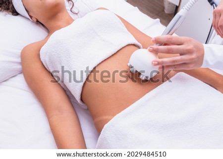 Cropped shot of a professional dermatologist performing radiofrequency lifting procedure on the stomach of a woman. Female client getting rf-lifting treatment on her belly at cosmetology clinic
